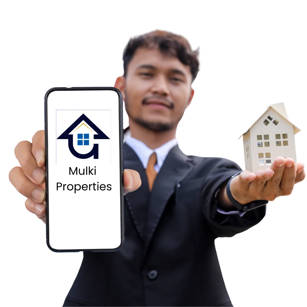 A man in a suit holding a smartphone displaying the Mulki Properties logo along with a miniature house model